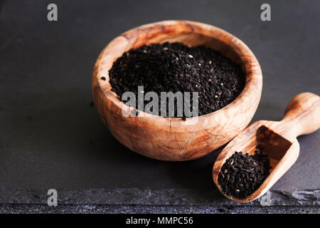 Il cumino nero o nigella sativa o kalonji semi nella ciotola con il cucchiaio sul nero ardesia sfondo, il fuoco selettivo Foto Stock