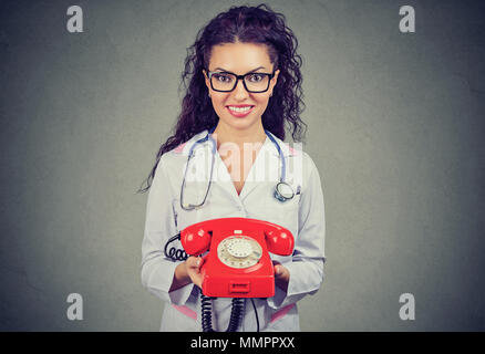 Donna sorridente medico tenendo un telefono pronto a rispondere alle chiamate telefoniche, fornire servizio medico Foto Stock