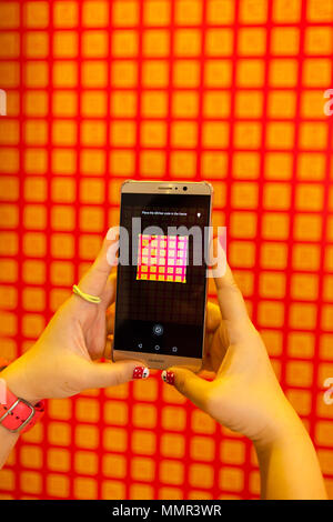 Una signora della mano che tiene un telefono intelligente per eseguire la scansione di codice QR sulla parete Foto Stock