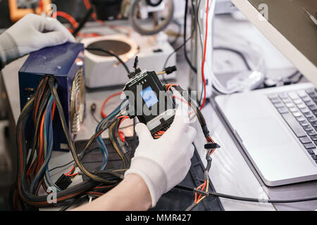 Lavorare con l'alimentazione del calcolatore. Dispositivo di microelettronica. Close-up mani di un lavoratore di servizio riparazione dei PC moderni. La riparazione e il concetto di servizio. Foto Stock