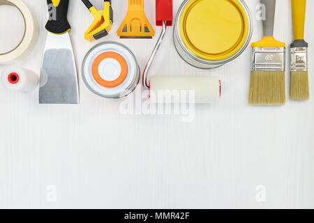 Barattoli di vernice, spazzole, coltello da stucco e sui rulli di legno bianco sullo sfondo di superficie, vista dall'alto Foto Stock