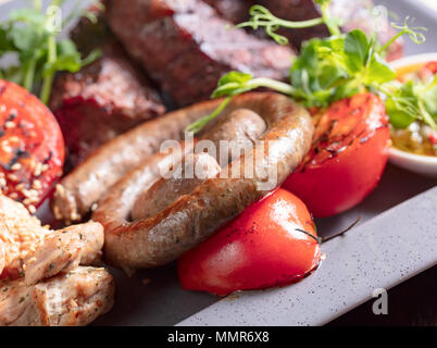 Un assortimento di deliziose grigliate di carne e salsicce con verdure e verdi . Foto Stock