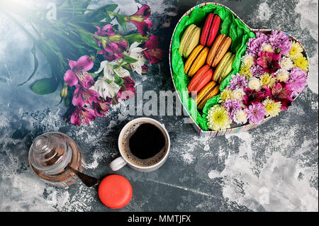 Confezione regalo a forma di cuore con fiori e amaretti, una tazza di caffè e un mazzo di fiori su un sfondo di calcestruzzo. Facile tonificante. Vista dall'alto. Foto Stock