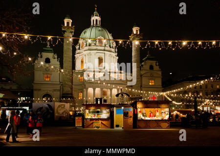 Sera atChristmas mercato davanti di Vienna la Karlskirche con illuminazione festosa, si spegne e si accende la spia chiesa barocca in background Foto Stock