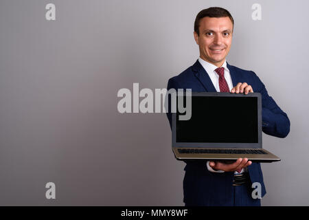 Imprenditore indossare tuta mentre holding laptop contro backg grigio Foto Stock