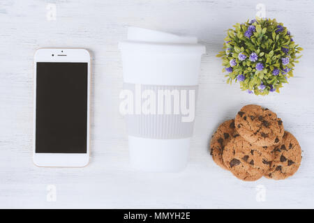 Vista superiore della schermata vuota mobile con una tazza di plastica di caffè con manicotto e cookie sul bianco sullo sfondo di legno Foto Stock