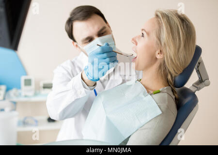 Vista laterale della ragazza seduta nella poltrona mentre il dentista con piccolo specchio ad esplorare i denti le condizioni. Foto Stock