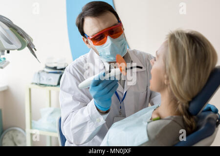 Professional dentista dente di riempimento e usando luce ultravioletta lavora con la donna in armadio. Foto Stock