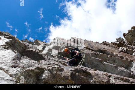 Maschio guida di montagna rappelling off una ripida roccia sotto un bel cielo blu con nuvole bianche Foto Stock