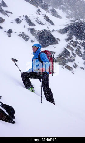 Maschio paese indietro sciatore di affrontare una salita con forte couloir nella neve profonda durante forti nevicate in inverno Foto Stock