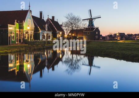 Case in legno e il mulino a vento sono riflesse nelle acque blu del fiume Zaan Zaanse Schans Olanda settentrionale dei Paesi Bassi in Europa Foto Stock