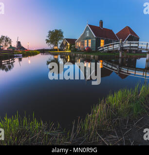 Case in legno e il mulino a vento sono riflesse nelle acque blu del fiume Zaan Zaanse Schans Olanda settentrionale dei Paesi Bassi in Europa Foto Stock