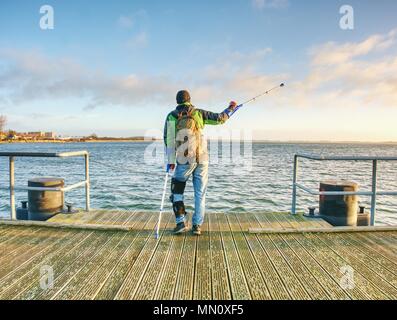 Uomo con le stampelle sulla mole Pier. Turistico con gamba rotta su stampelle. Viaggiatore con ferire una gamba in bende. Lunghezza completa di uomo con gamba rotta. Foto Stock