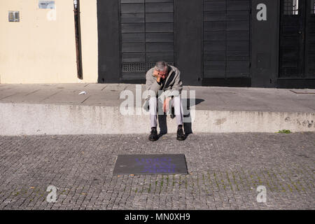 Un uomo si siede da solo tenendo la sua testa in una strada a Porto, Portogallo Foto Stock