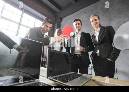 La gente di affari giocare a ping pong sul tavolo per ufficio con computer portatili Foto Stock