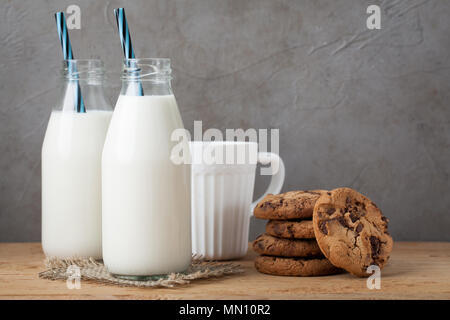 Due bottiglie di latte e biscotti al cioccolato su sfondo scuro con spazio di copia Foto Stock