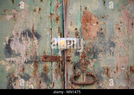 Pelati in legno porta bloccata in background con maniglia arrugginita e un lucchetto. Trito marrone, verde ingresso fornisce la sicurezza e la privacy. Vista ravvicinata con det Foto Stock