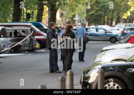 14 maggio 2018, Germania Berlino: poliziotti stare accanto a bruciate le vetture a Kollwitzplatz nel quartiere di Prenzlauer Berg. Nelle prime ore del mattino undici vetture bruciate. Auto parcheggiata presso il vicino Knaackstrasse erano anche innescata. Dal momento che un politico di motivare si presume lo stato di protezione di Office è responsabile dell'inchiesta. Foto: Paolo Zinken/dpa Foto Stock