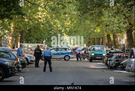 14 maggio 2018, Germania Berlino: poliziotti stare accanto a bruciate le vetture a Kollwitzplatz nel quartiere di Prenzlauer Berg. Nelle prime ore del mattino undici vetture bruciate. Auto parcheggiata presso il vicino Knaackstrasse erano anche innescata. Dal momento che un politico di motivare si presume lo stato di protezione di Office è responsabile dell'inchiesta. Foto: Paolo Zinken/dpa Foto Stock