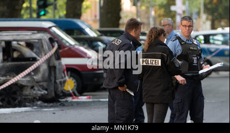 14 maggio 2018, Germania Berlino: poliziotti stare accanto a bruciate le vetture a Kollwitzplatz nel quartiere di Prenzlauer Berg. Nelle prime ore del mattino undici vetture bruciate. Auto parcheggiata presso il vicino Knaackstrasse erano anche innescata. Dal momento che un politico di motivare si presume lo stato di protezione di Office è responsabile dell'inchiesta. Foto: Paolo Zinken/dpa Foto Stock