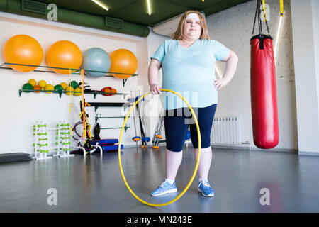 A piena lunghezza Ritratto di soggetti obesi giovane donna in posa con hula hoop durante la formazione weightloss in palestra, spazio di copia Foto Stock