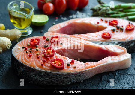 Due crudo fresco filetti di salmone con spezie e verdure: asparagi pomodori, lo zenzero, i calli di pepe, sale e pepe, peperoncino, limone e olio di oliva su nero ba Foto Stock