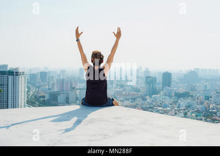 Uomo seduto sul tetto nero e mostra fino a mano con cielo blu di sfondo e sunshine,combattimenti uomo sul tetto Foto Stock