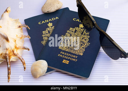 Piatto due laici passaporto canadese con occhiali da sole e conchiglie su cartoncino bianco dello sfondo. Vista dall'alto. Viaggio concetto creativo Foto Stock