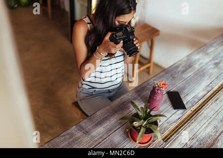 Donna di scattare le foto di un smoothie posto accanto a un vaso di fiori utilizzando una telecamera professionale per il suo cibo blog. Blogger alimentare a scattare foto per il suo blog Foto Stock