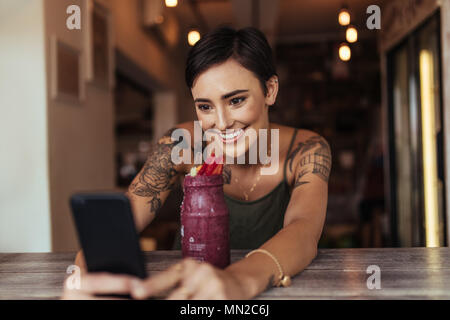 Donna sorridente prendendo un selfie con un smoothie collocato di fronte a lei utilizzando un telefono cellulare per il suo cibo blog. Blogger alimentare a scattare foto per il suo blog Foto Stock