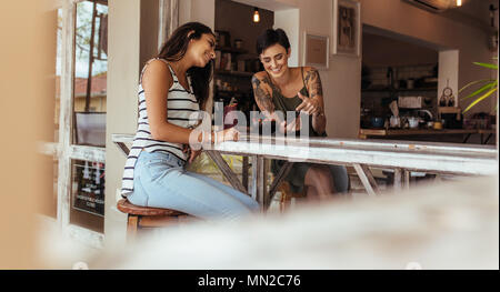 Amici guardando le foto nel telefono cellulare mentre è seduto a casa con una coppa di frutta e frullati sul tavolo. Due donne blogger di condividere idee su flood Foto Stock