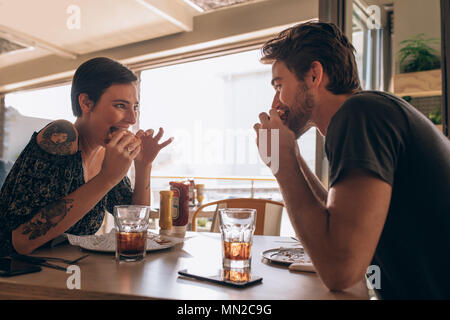 Coppia giovane Godendo mangiando burger insieme. Donna sorridente mangiare hamburger con il suo fidanzato in un ristorante. Foto Stock
