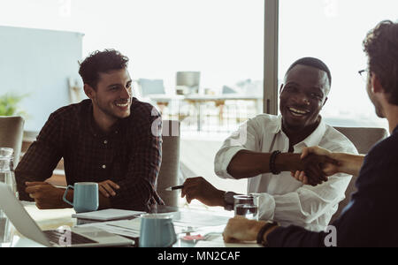 Discutere gli imprenditori lavorano seduti ad un tavolo per conferenza in ufficio. Gli uomini si stringono la mano e sorridente durante una riunione di affari. Foto Stock