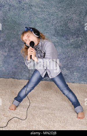 Bellissima bambina con microfono a casa cantando Foto Stock