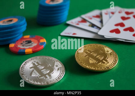 Due bitcoins recante sul verde tavolo del poker e il mazzetto di chip con carte in background|Oro|argento|blue|a filo Foto Stock