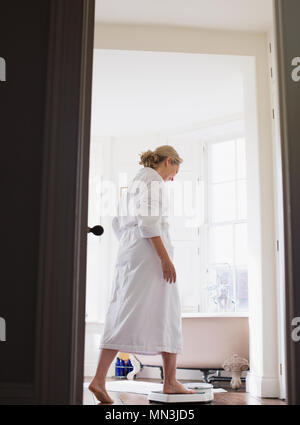 Donna matura in accappatoio intensificazione su una bilancia da bagno Foto Stock