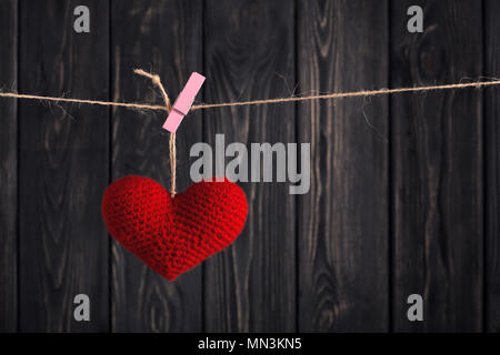 Fatte a mano cuore rosso appeso alla corda con clothespin sul grigio scuro dello sfondo di legno. Buon San Valentino festa. Il messaggio di amore concetto Foto Stock