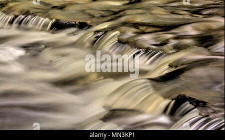 Un primo piano di una piccola cascata che mostra tutti gli intricati movimento dell'acqua che cade e volute sulle rocce in streambed. Elaborati come un Foto Stock