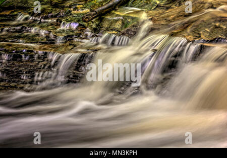 Un primo piano di una piccola cascata che mostra tutti gli intricati movimento dell'acqua che cade e volute sulle rocce in streambed. Elaborati come un Foto Stock