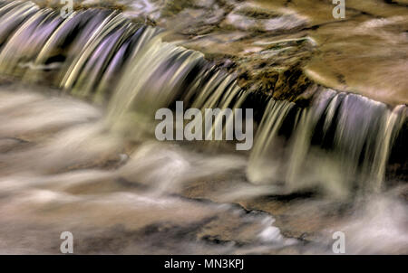 Un primo piano di una piccola cascata che mostra tutti gli intricati movimento dell'acqua che cade e volute sulle rocce in streambed. Elaborati come un Foto Stock