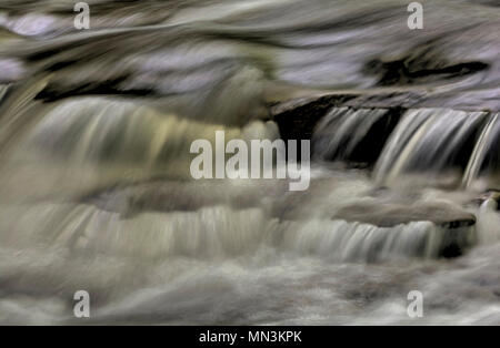 Un primo piano di una piccola cascata che mostra tutti gli intricati movimento dell'acqua che cade e volute sulle rocce in streambed. Elaborati come un Foto Stock