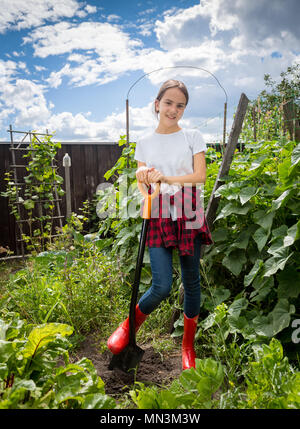 Bella ragazza sorridente con la pala in piedi in giardino Foto Stock