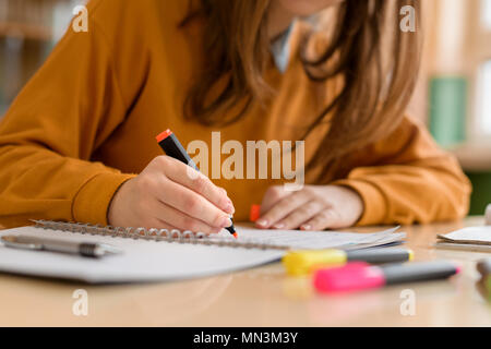 Giovane femmina irriconoscibile studente di college in classe, prendere appunti e utilizzare evidenziatore. Studente focalizzato in aula. Autentico concetto di istruzione. Foto Stock