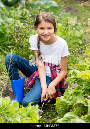 Bella ragazza sorridente spudding terra con piccola cazzuola in giardino Foto Stock