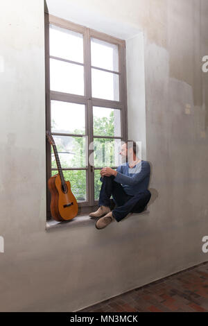 La malinconia musicista seduto accanto a una finestra Foto Stock