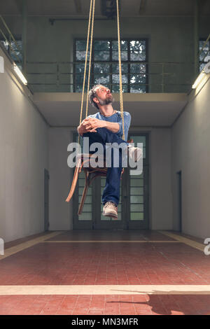 Uomo seduto su una sedia pensile Foto Stock