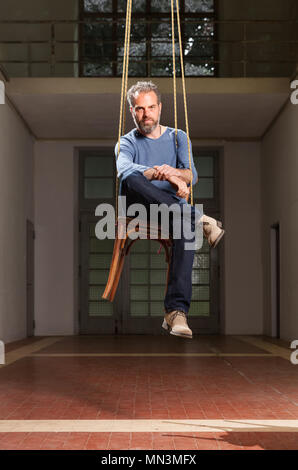 Guy hanging seduto sulla sedia, vecchio spazio industriale sfondo Foto Stock