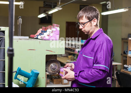 Un giovane lavoratore di sesso maschile rende la suola delle calzature per bambini realizzato in vera pelle con una speciale macchina nel laboratorio di cucito Foto Stock