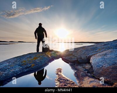 Silhouette di un solo uomo che guarda verso la vibrante del tramonto. Flare e riflessi in acque poco profonde del livello del mare Foto Stock