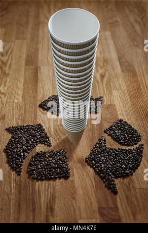 I chicchi di caffè formando simbolo di riciclaggio intorno al pacco di riciclabile tazze di caffè Foto Stock
